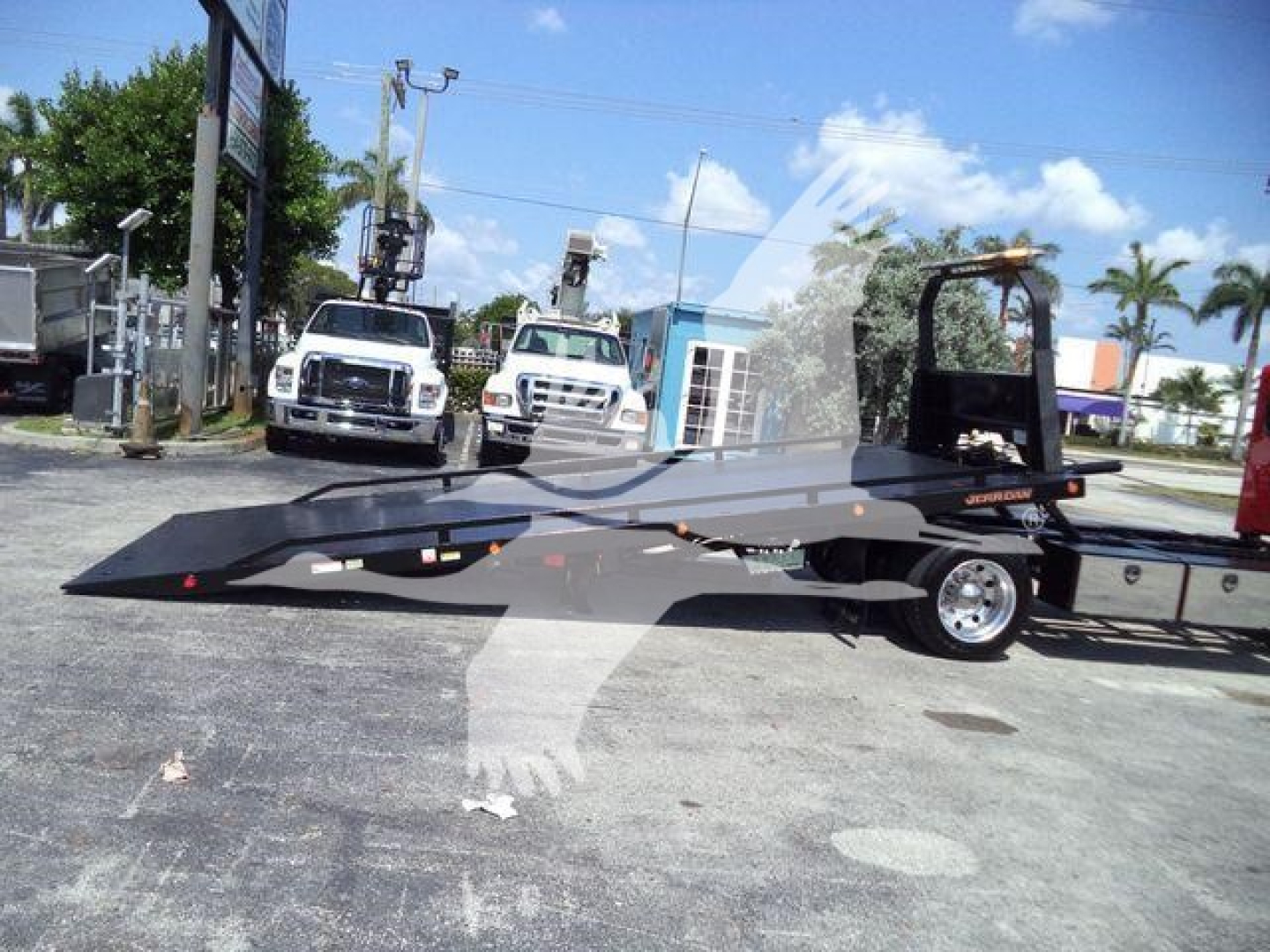 Peterbilt 337 rollback truck with a long flatbed and hydraulic equipment, in a dealership lot with other trucks in background.