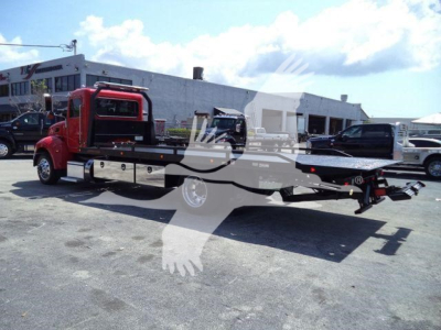 Red Peterbilt 337 rollback tow truck with long flatbed in a dealership lot; stock number T21864 visible in listing context.