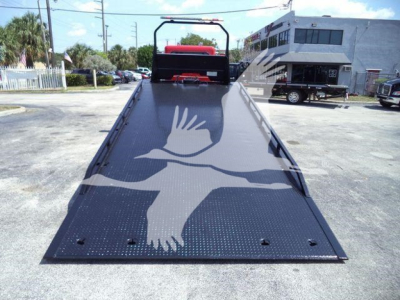 Peterbilt 337 rollback truck with a flatbed ramp and white bird logo on the metal surface, showing the rear platform and surrounding lot.
