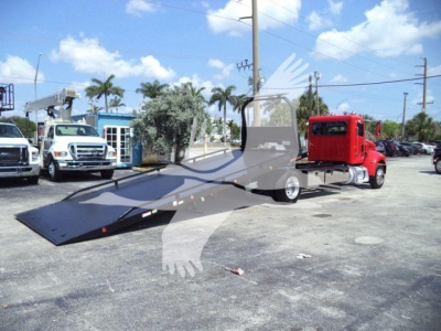 Peterbilt 337 rollback tow truck with long flatbed and red cab, parked in a lot.