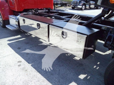 Truck undercarriage showing chrome fuel/transmission toolbox with two rectangular compartments and latching handles; reflection of light on polished surface.
