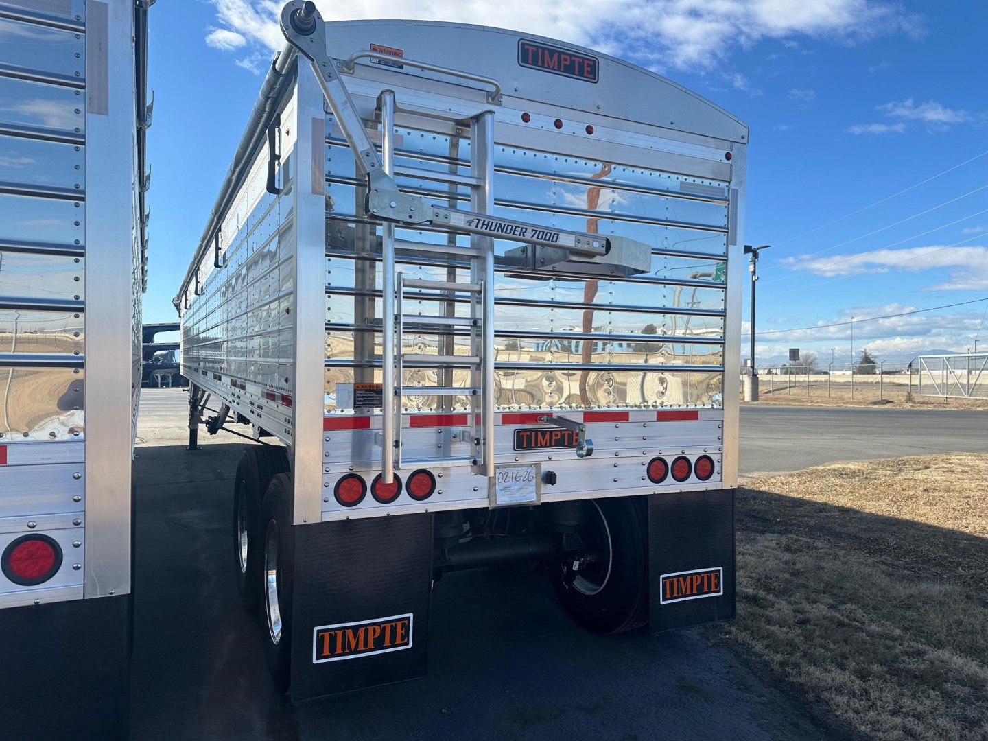 Trailer rear view showing Timpe brand logo, ladder gates, and aluminum side panels on a new Timpte Super Hopper W trailer. Visible text includes TIMPTE on rear, Thunder Lift 1000 label, and mudflaps with TIMPTE.
