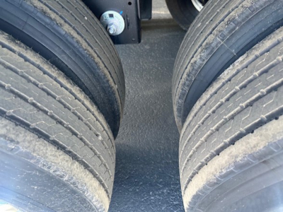 Trailer dual rear wheels view showing tires and frame undercarriage near suspension and a blue cap in background