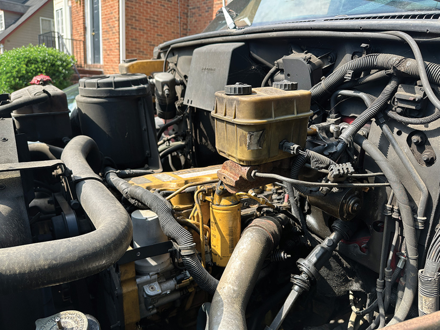 Chevrolet 6500 engine bay with visible coolant reservoir and yellow engine components, hoses, and wiring in a rollback truck.