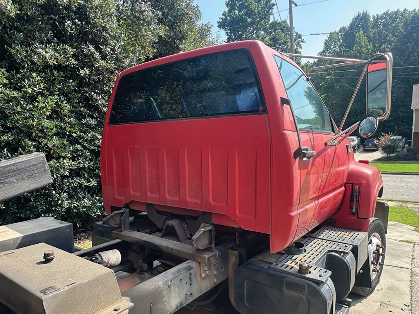 Truck cab rear and side view showing red Chevrolet 6500 rollback with open driver door and chassis behind cab; VIN plate visible may be inside but not legible.