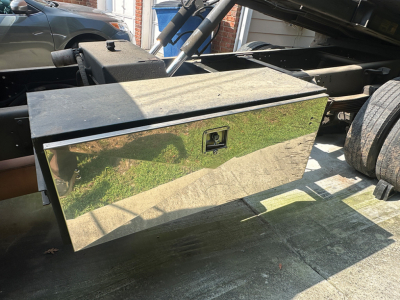 Flatbed truck toolbox/chest mounted on a rollback chassis showing a polished metal diamond-plate storage box with a handle latch.