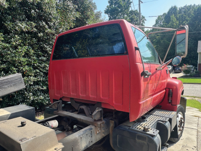 Truck cab rear and side view showing red Chevrolet 6500 rollback with open driver door and chassis behind cab; VIN plate visible may be inside but not legible.