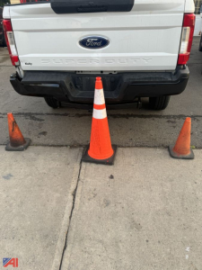 Ford F-250 Super Duty rear view showing tailgate with 'FORD' emblem and 'SUPER DUTY' lettering, four traffic cones behind on pavement.