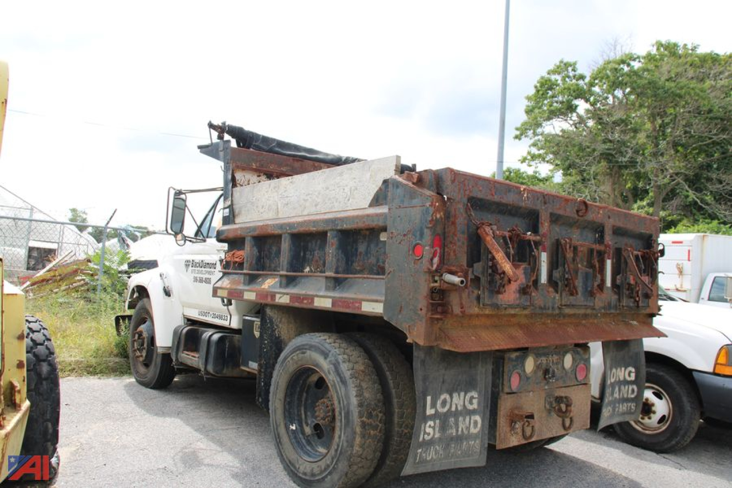 Ford F-800 dump truck rear view showing rusted dump bed and taillights, white cab, long island mudflaps, and a VIN placard likely on the dash area.