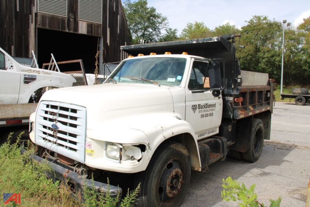 Ford F-800 dump truck in-service with white cab and black dump bed, front grille and headlights visible, some front-end damage, utility decals on door