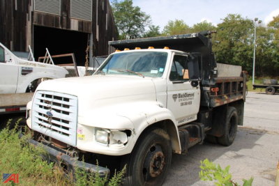 Ford F-800 dump truck in-service with white cab and black dump bed, front grille and headlights visible, some front-end damage, utility decals on door