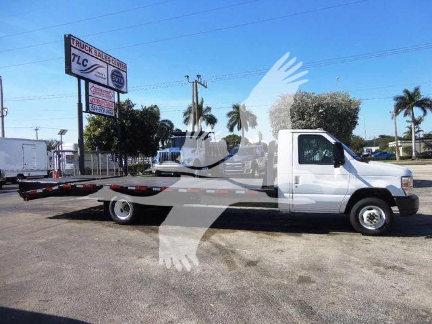 Flatbed tow truck side view of 2011 Ford E450 showing long flatbed with white cab, on a dealership lot.