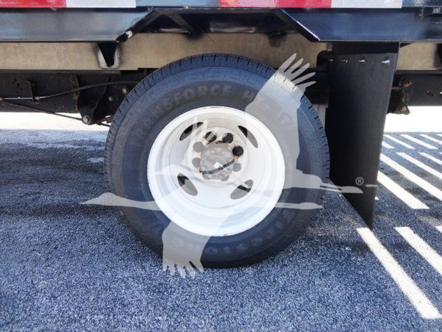 Flatbed truck rear wheel area with white steel rim and tire; visible undercarriage and mounting hardware