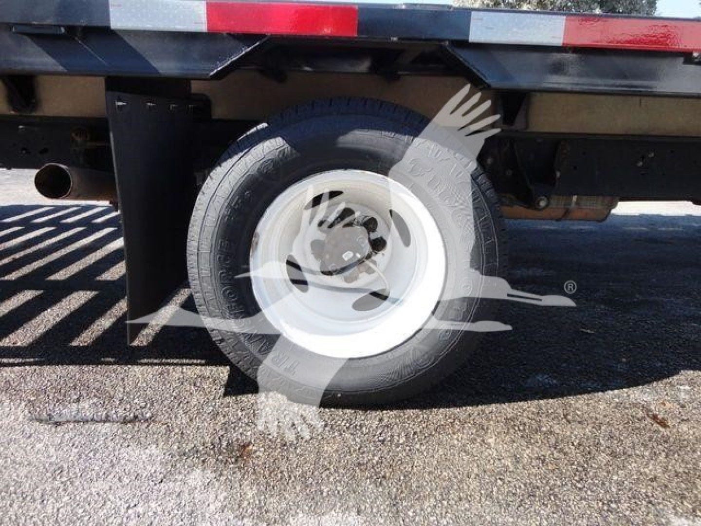 Ford E450 flatbed truck rear wheel and suspension showing wheel, tire, and undercarriage components.