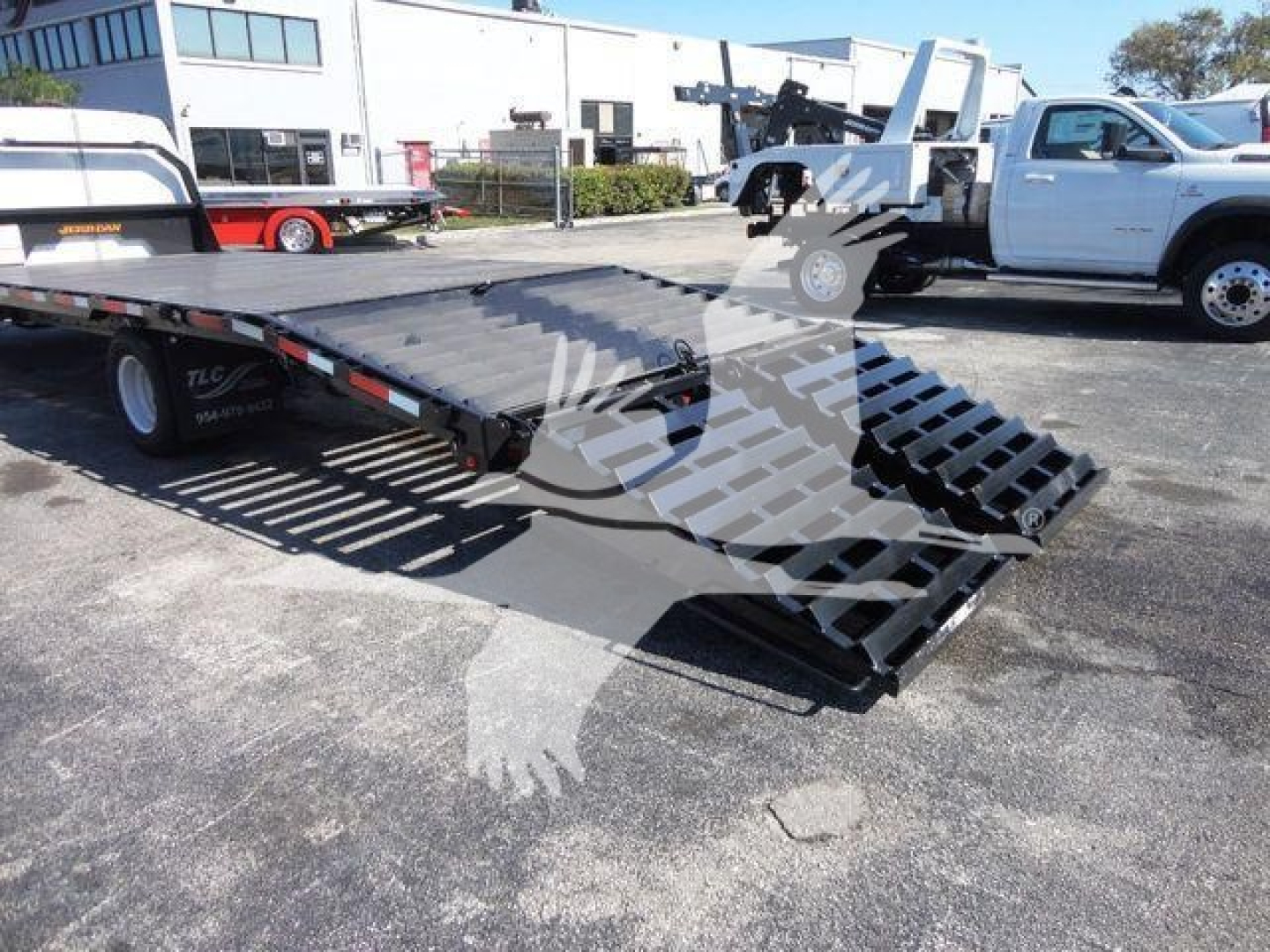 2011 Ford E450 flatbed tow truck with ramped bed and hydraulic loading ramps in a dealership lot.