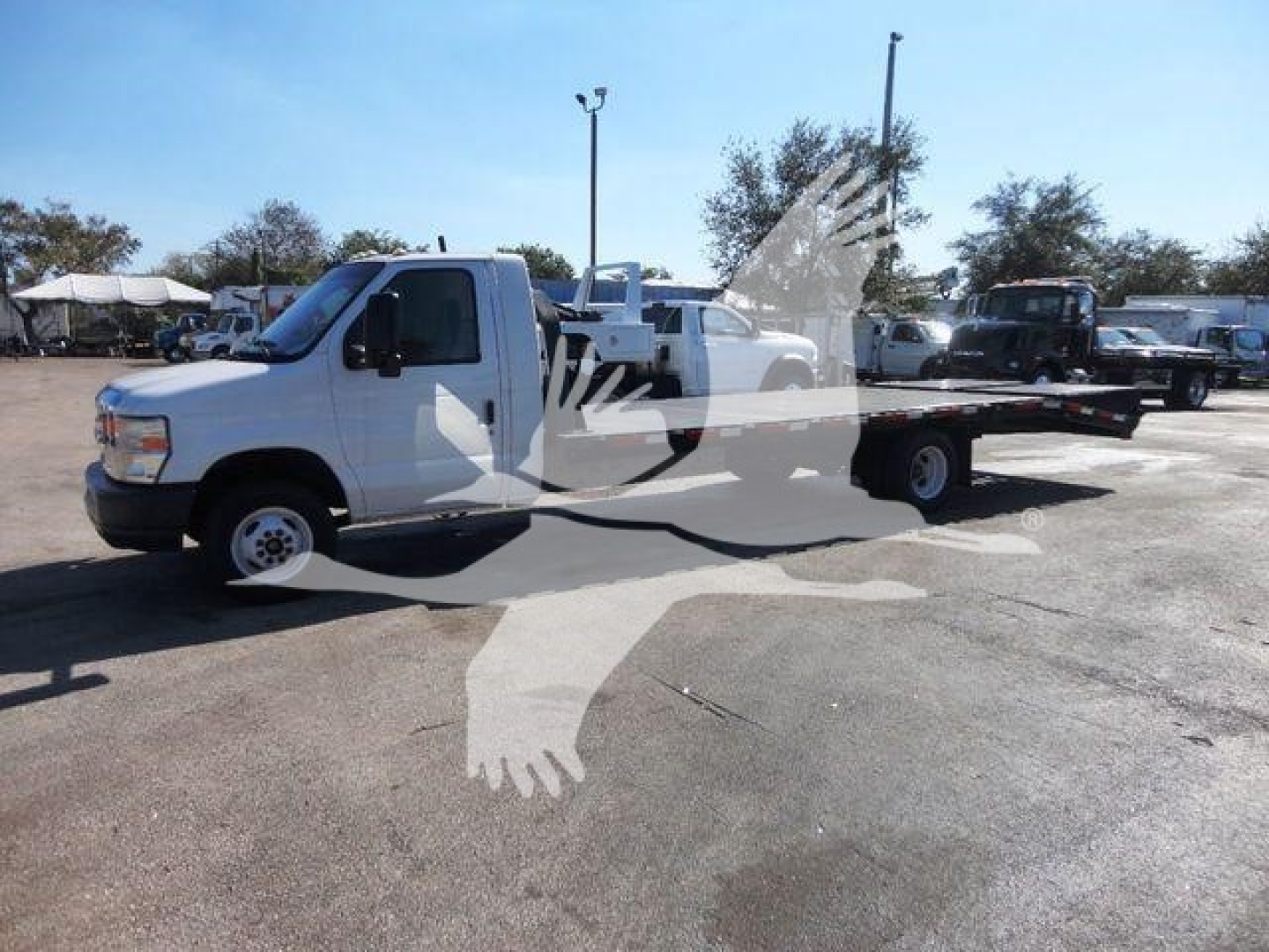 Truck in a lot showing a white 2011 Ford E450 flatbed tow truck with extended flatbed and cab visible.
