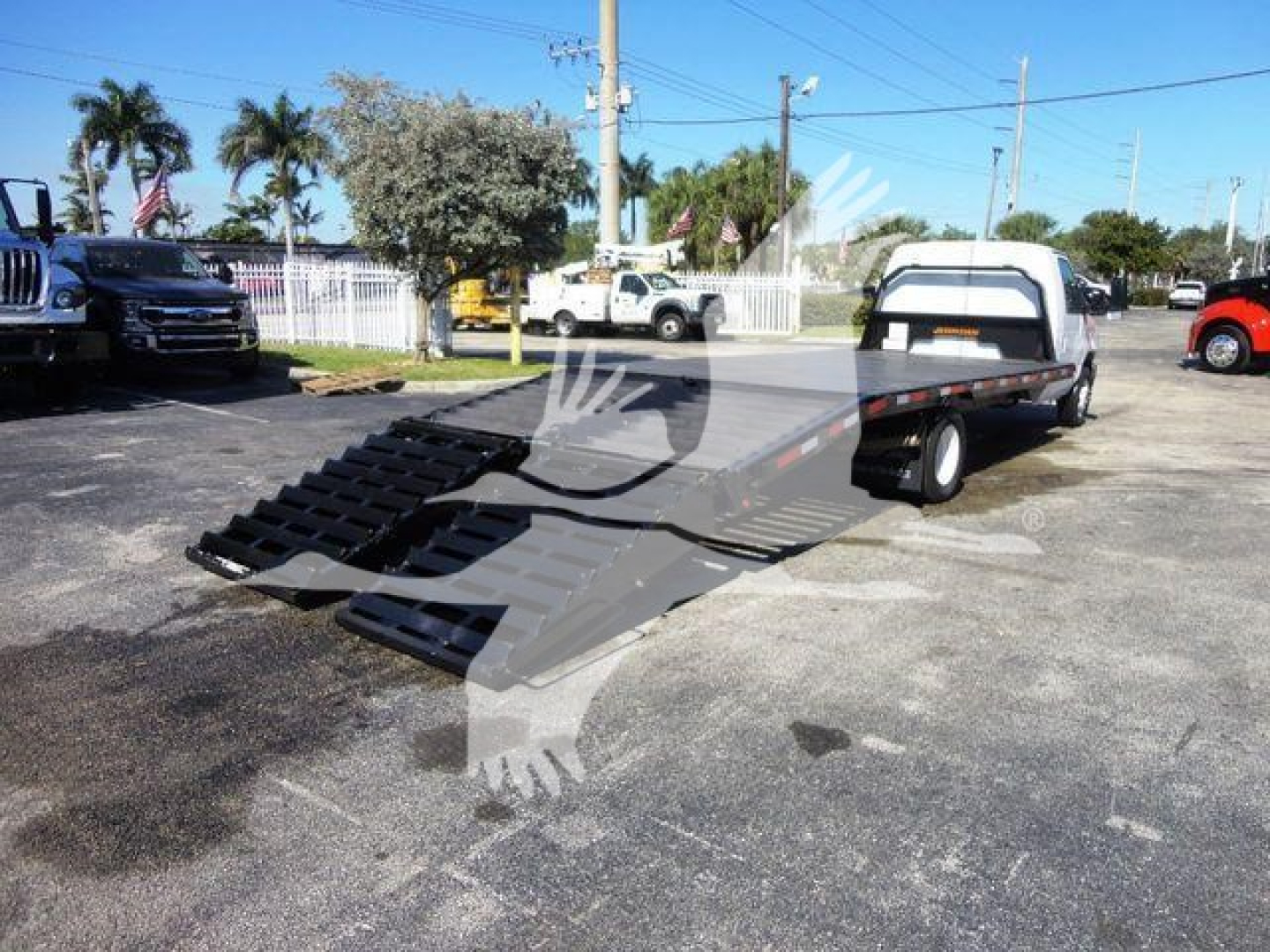 Flatbed tow truck with lowered ramp system and extended flatbed on a service lot.