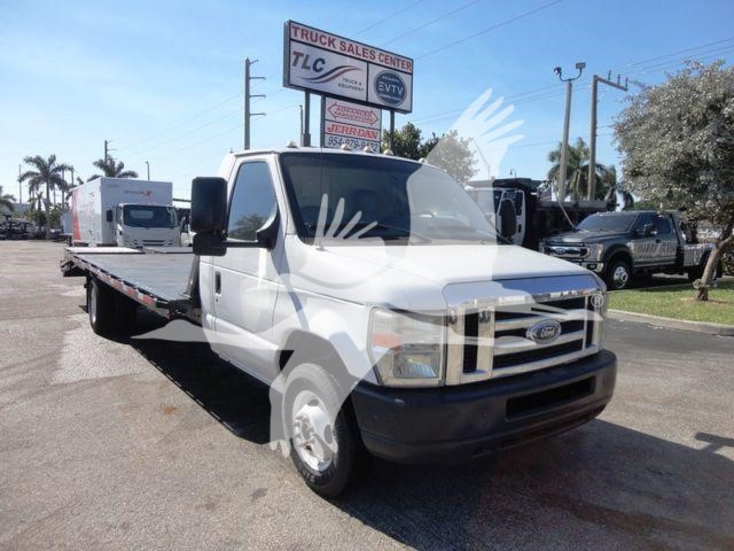 Flatbed tow truck showing Ford E-450 cab with long flatbed, front grille, headlights; dealership lot in background with signs.
