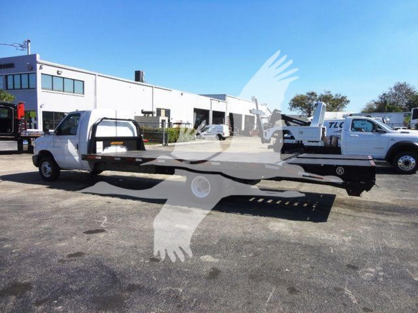 Flatbed tow truck on a sunny lot, side view showing long flatbed and wheel arches.