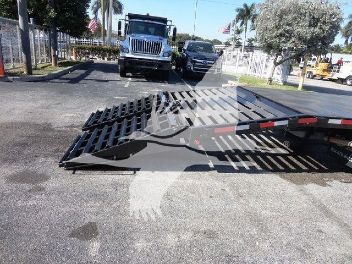 Ford E450 flatbed truck in yard with loading ramp deployed and trailer bed visible.