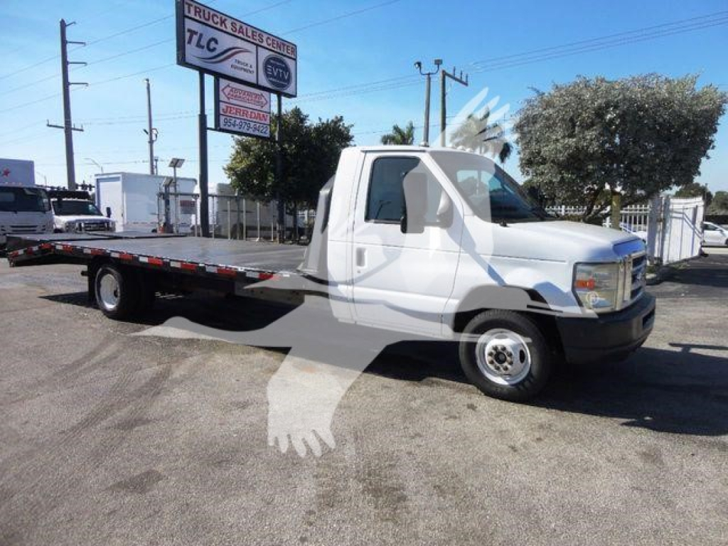 Flatbed tow truck, white Ford E-450 with extended cab, long flatbed, side view in a dealership lot.
