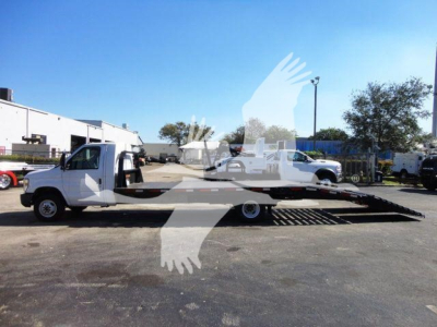 Flatbed tow truck on ramp bed with empty wheel-lift, 2011 Ford E450 in service showing side view and stock lot background.