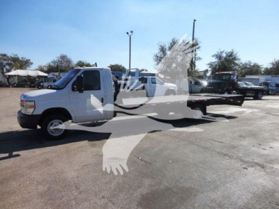 Flatbed tow truck in a lot with a white 2011 Ford E450 and a long flatbed visible; other trucks in background.