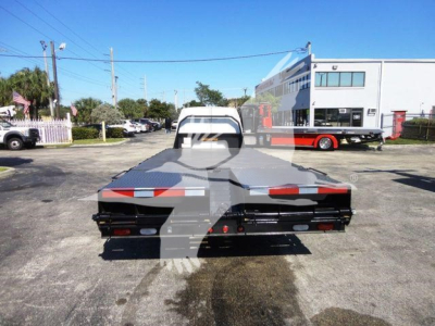Flatbed tow truck seen from rear with reflective chevrons and lights; Ford E-450 flatbed with loading area; dealership building in background.
