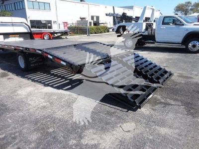 2011 Ford E450 flatbed tow truck with ramped bed and hydraulic loading ramps in a dealership lot.