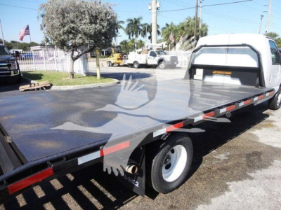 Ford E450 flatbed tow truck with long steel flatbed and white cab, rear wheels, and safety reflectors visible.