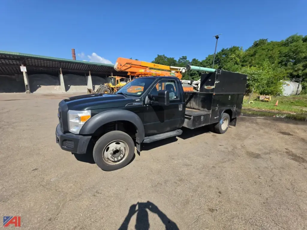 Ford F-550 Super Duty utility truck with service bed and crane, black exterior, side view showing front grille and wheel, daylight outdoor lot