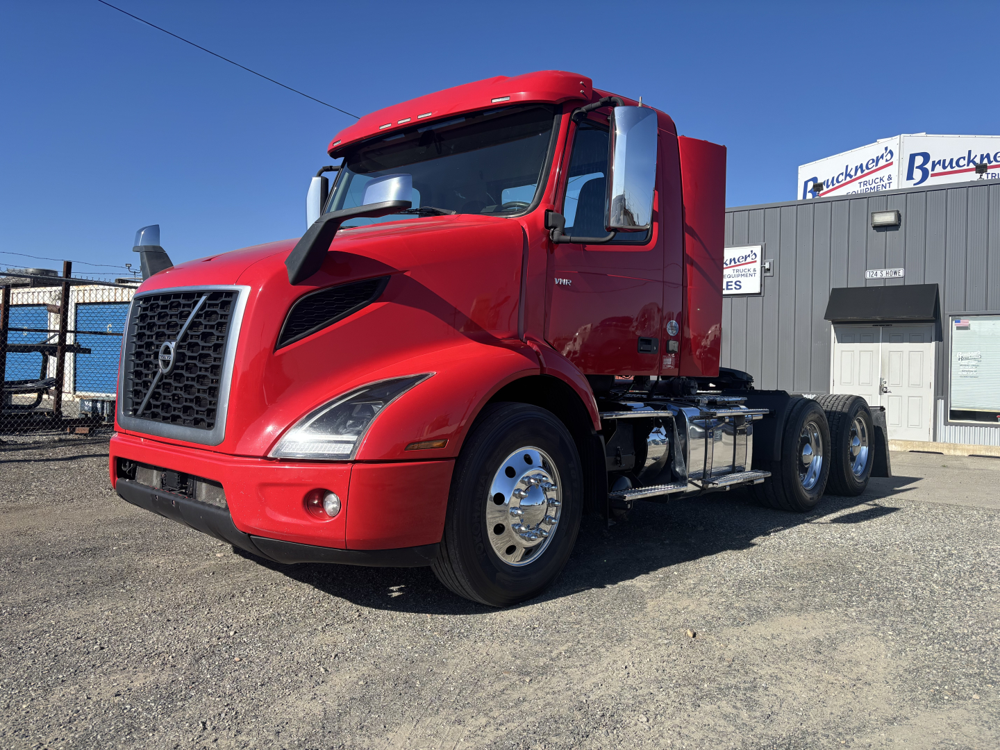 Volvo VNR64T300 conventional daycab tractor in red, front three-quarter view showing grille, cab, dual rear axles, chrome fuel tanks, and wheels.