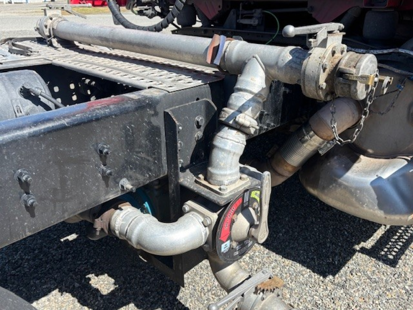 Rear chassis area of a 2023 Volvo VNR truck showing hydraulic lines, piping, and a circular red-and-black component with hoses.