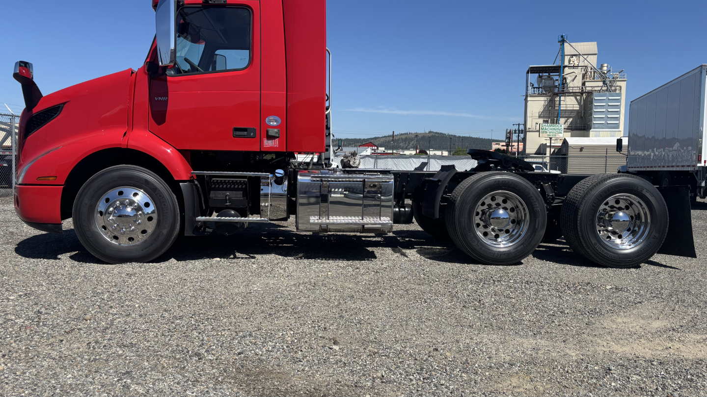Side view of a red Volvo VNR64T300 daycab truck chassis showing fuel tank, exhaust, and rear axles.