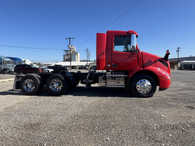 Side view of a red 2023 Volvo VNR truck tractor with a two-axle rear, chrome wheels, and fuel/maintenance compartments.
