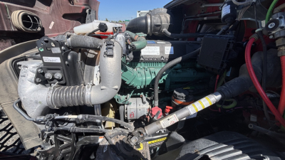 Volvo VNR64T300 engine bay showing diesel engine with hoses, belts, and wiring; visible green engine block and intake manifold; various labels on components.