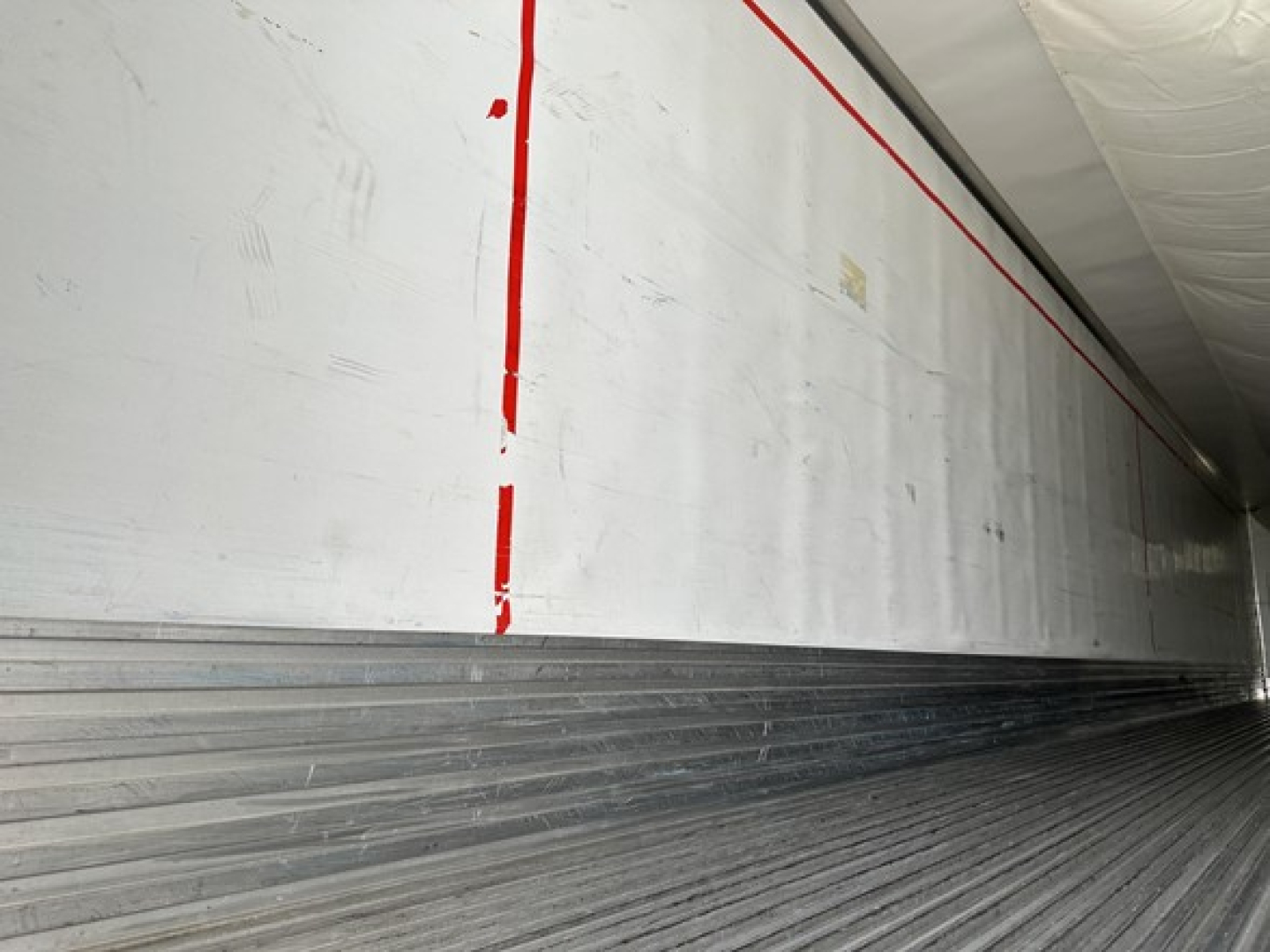 Trailer interior wall with aluminum siding and ribbed floor showing red vertical line markings.