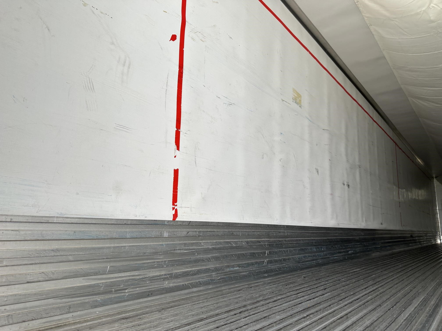 Trailer interior wall with vertical red stripes and ribbed metal floor; no legible model text visible.