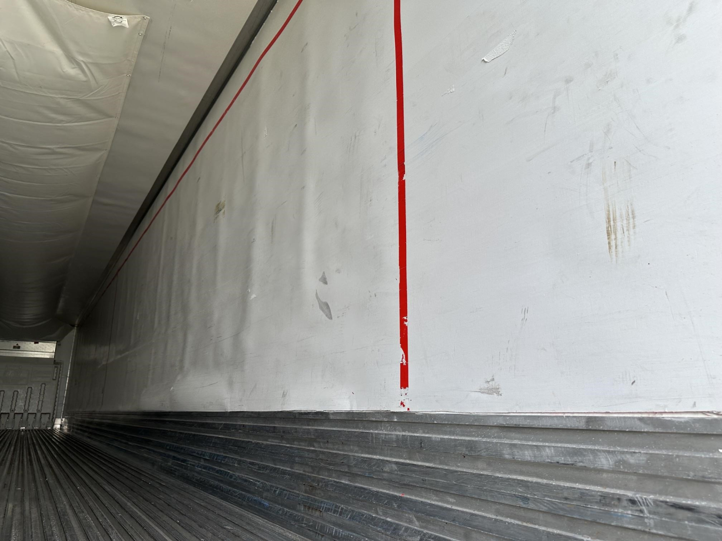 Trailer interior wall with vertical red stripe and ribbed flooring showing utility reefer trailer branding lines.