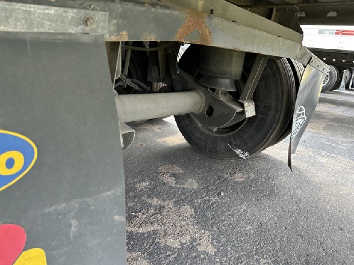 Trailer underside showing wheel hub and suspension of a 2015 Utility 3000R reefer trailer with some rust on frame, dirt on ground, and a mudflap visible.