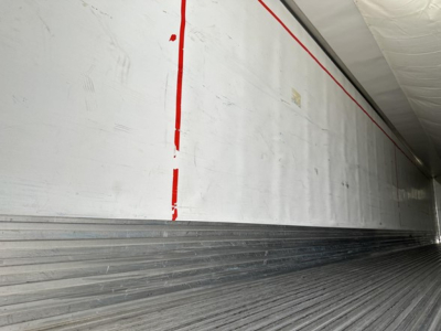 Trailer interior wall with aluminum siding and ribbed floor showing red vertical line markings.