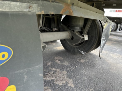 Trailer underside showing wheel hub and suspension of a 2015 Utility 3000R reefer trailer with some rust on frame, dirt on ground, and a mudflap visible.