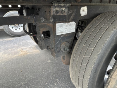 Rear undercarriage of a 2015 Utility 3000R trailer showing suspension brackets, frame, and wheel with a small identification plate on a rust-colored chassis.
