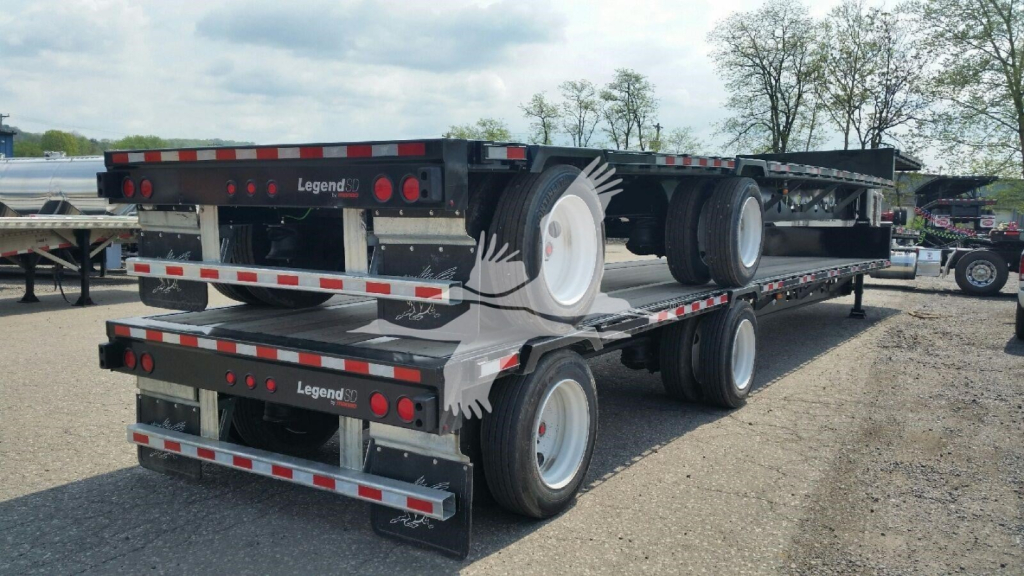 Manac drop deck trailer viewed from side with dual axles and spare tire mounted on neck area.
