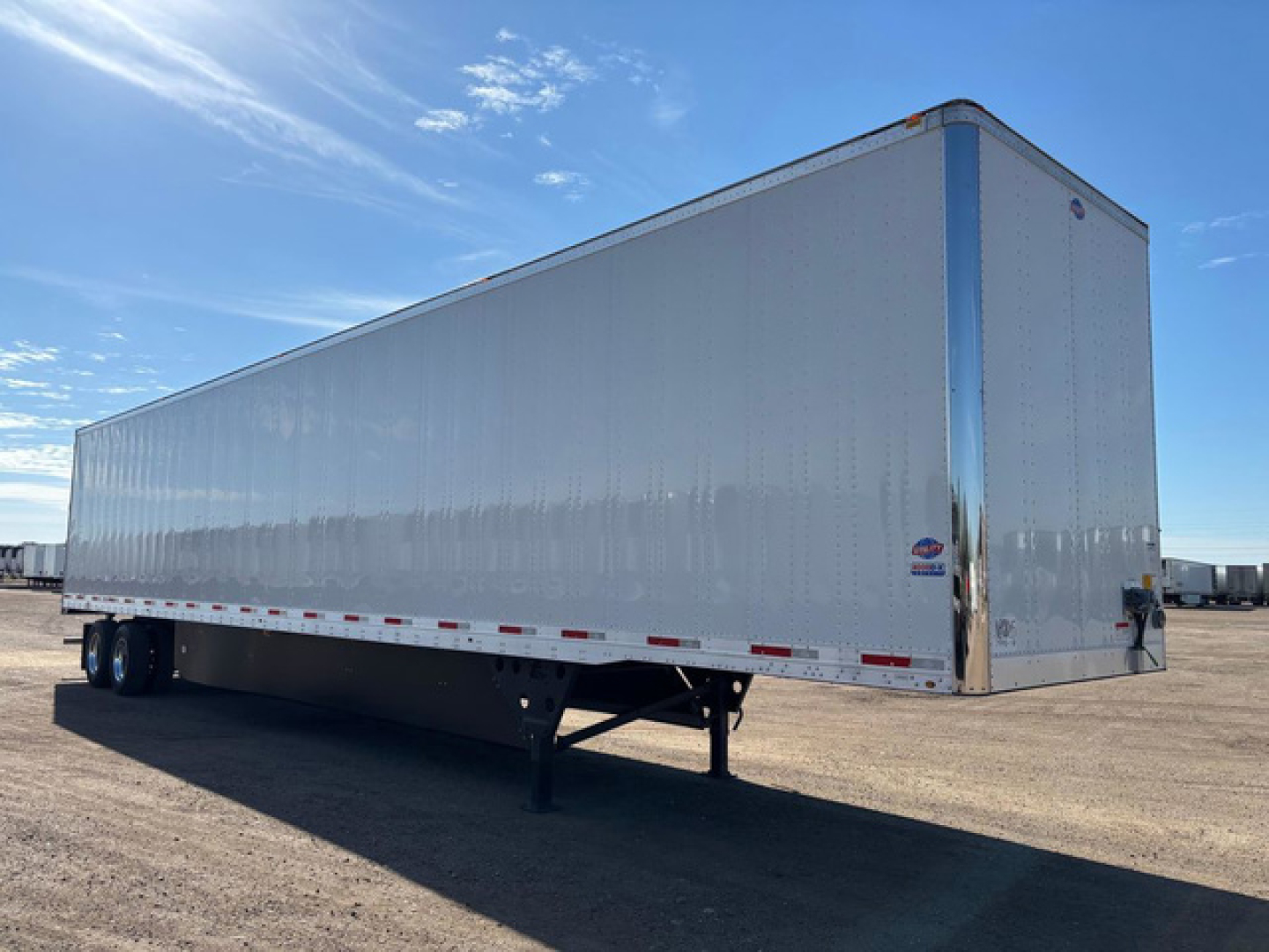 Utility dry van trailer showing long silver aluminum exterior with blue trim, front corner post, and landing gear. No visible text on the trailer surface.