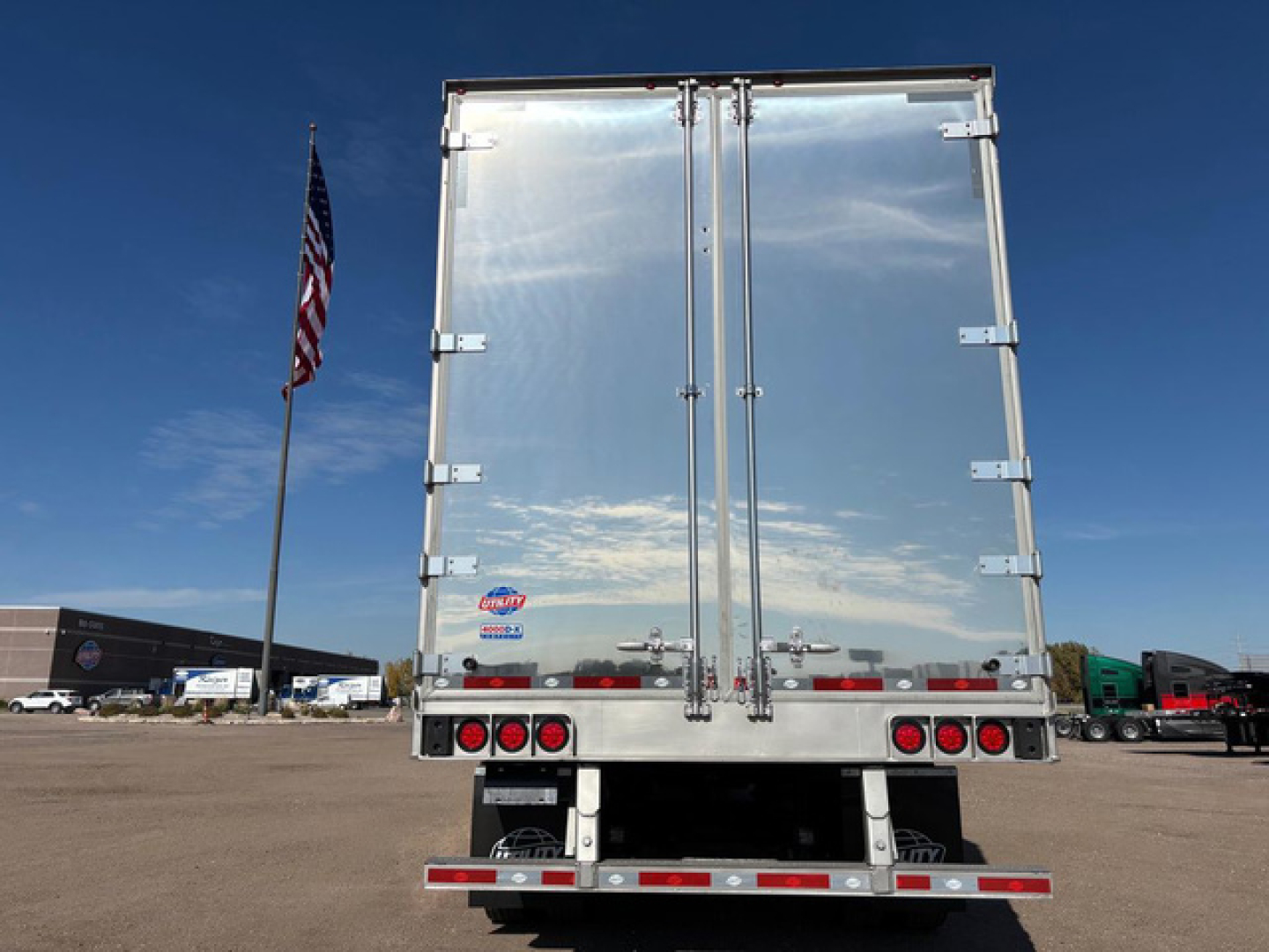 Rear view of a new 2027 Utility dry van trailer showing double rear doors with vertical bars and latches, red brake lights, bumper, and reflective tape.
