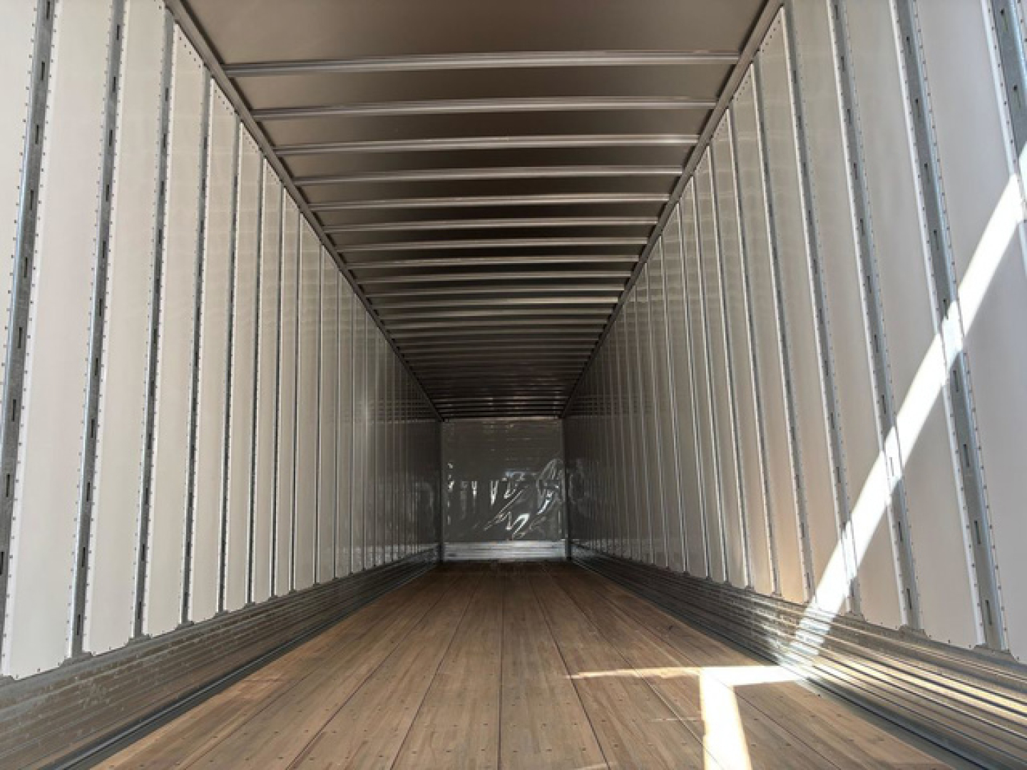 Trailer interior showing empty dry van cargo area with wood floor and metal walls and ceiling, straight length, light entering from door opening.