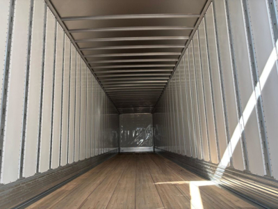 Trailer interior showing empty dry van cargo area with wood floor and metal walls and ceiling, straight length, light entering from door opening.