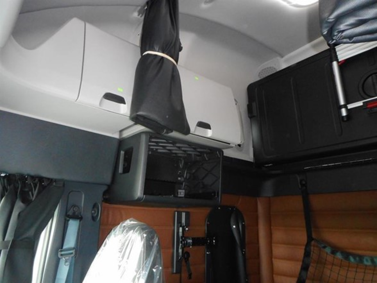 Cabin interior of a new Freightliner Cascadia 126, overhead storage compartments, covered seat, and glossy wood paneling on the sleeper area.