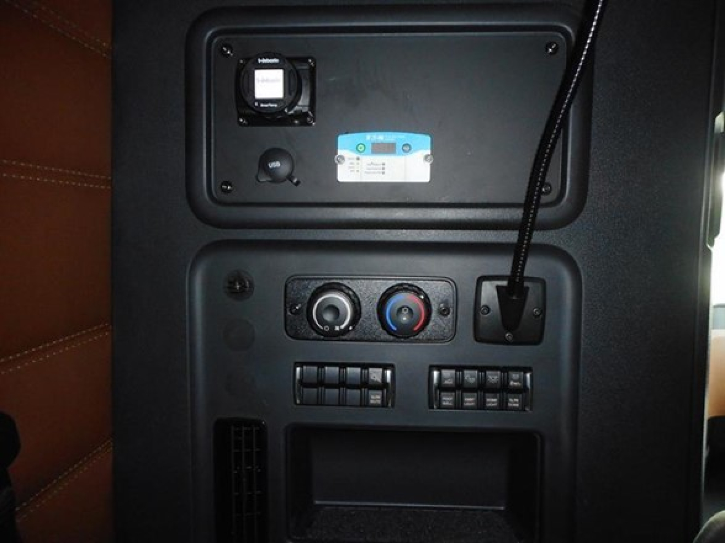 Truck cab interior panel with control knobs, vents, USB-like port, and a blue badge. Front overhead area shows a small square vent and circular knobs.